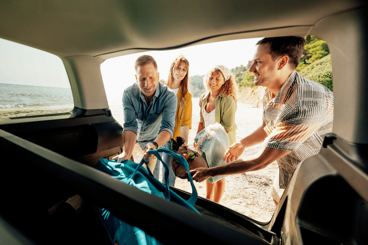 Amigos sacando sus pertenencias del maletero de un coche en la playa