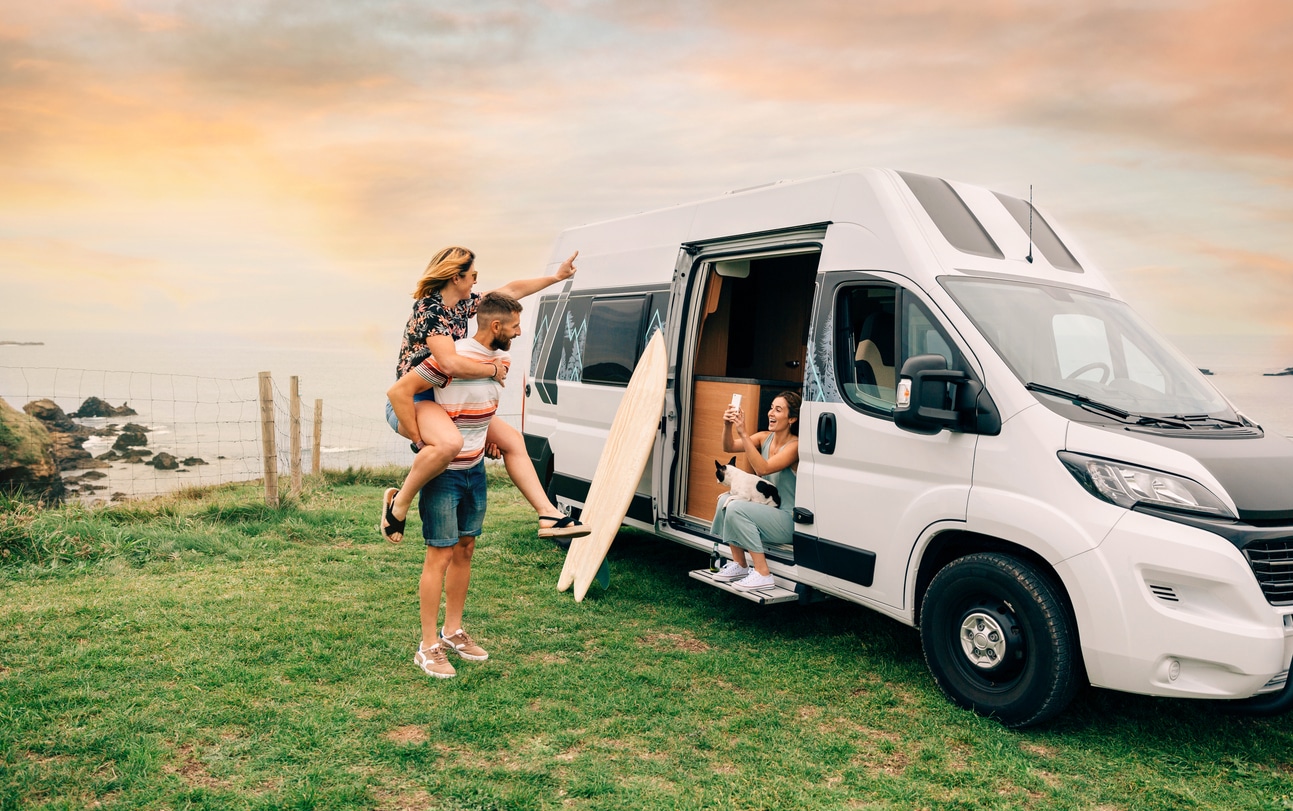 Una joven toma una foto con su teléfono celular de sus amigos divirtiéndose cabalgando junto a su camioneta camper durante un viaje