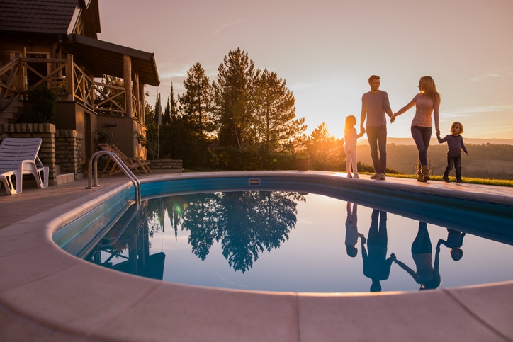 Loving family holding hands and walking by the pool at sunset.
